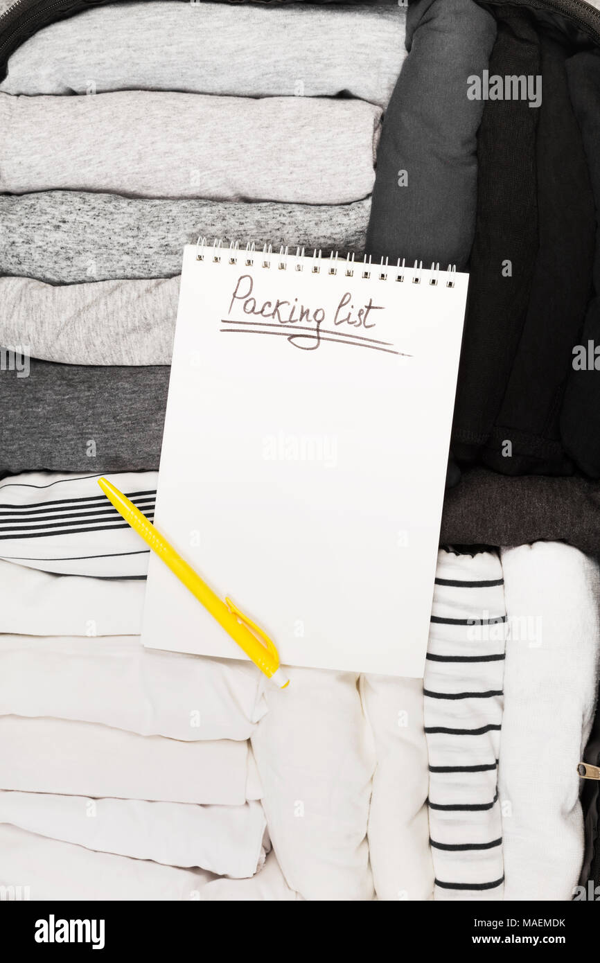 Confezionamento di abiti monocromatici in bianco e nero la valigia. Lista di imballaggio in bianco per notebook. Vista superiore, spazio di copia Foto Stock