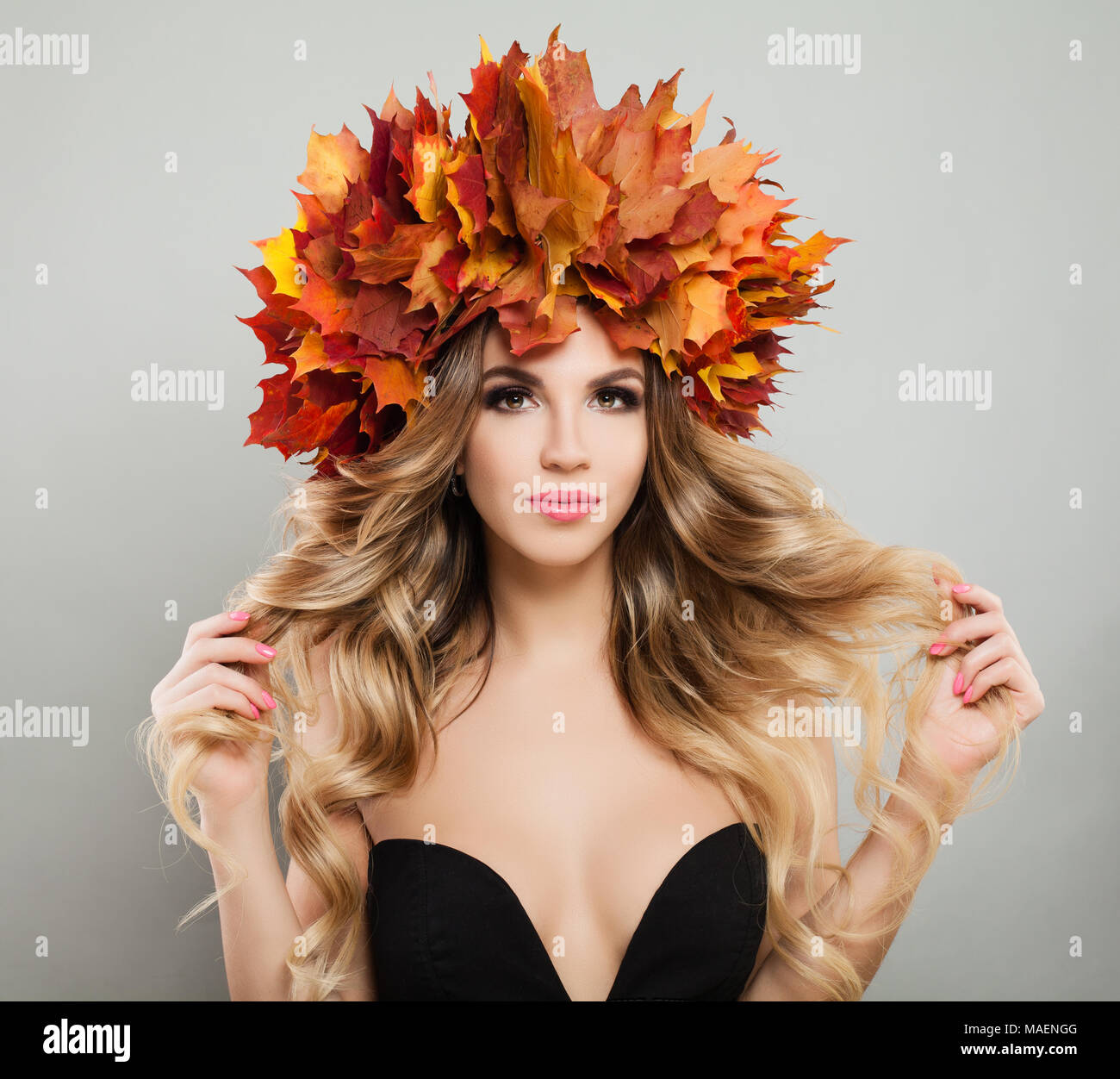 Bella giovane donna con foglie di autunno di toccare con la mano i suoi capelli. Modello di moda con il trucco, biondi capelli ricci e Ghirlanda di caduta Foto Stock