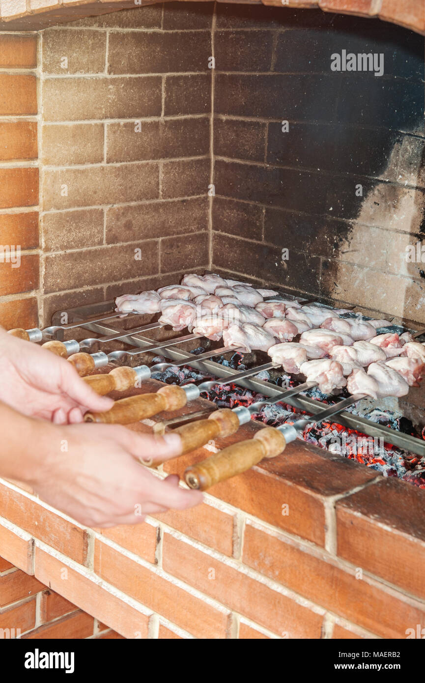 Mano trattiene gli spiedini con un delizioso, succosa kebab, fritti allo spiedo su un fuoco aperto in una pietra forno di casa. Il telaio verticale. Foto Stock