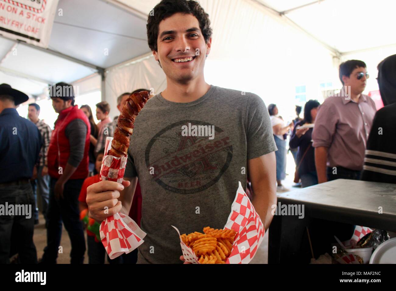 Un uomo godendo di salsiccia avvolta in bacon e waffle fries Houston Livestock e rodeo show 2018 STATI UNITI D'AMERICA Foto Stock