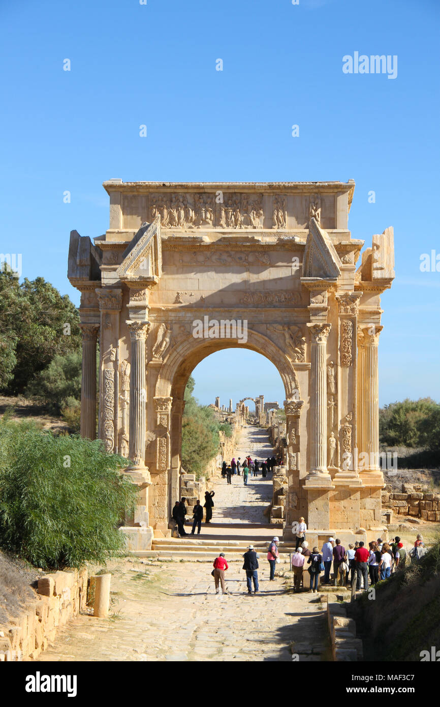 I turisti in piedi nella parte anteriore del ricostruito Arco di Settimio Severo all'entrata dell antica città romana di Leptis Magna, Tripoli, Libia Foto Stock