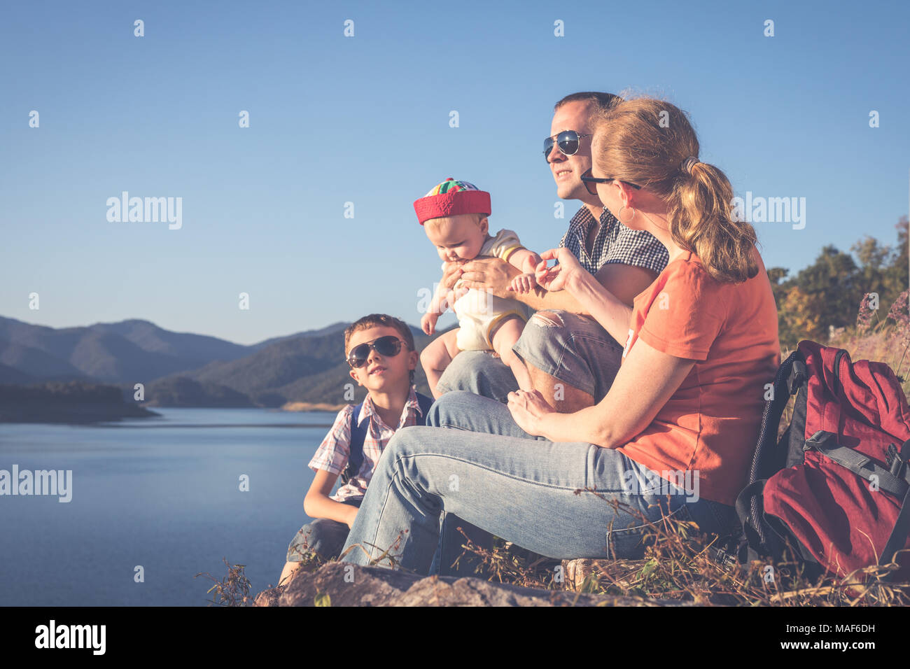 La famiglia felice seduto vicino al lago al giorno. Concetto di famiglia amichevole. Foto Stock
