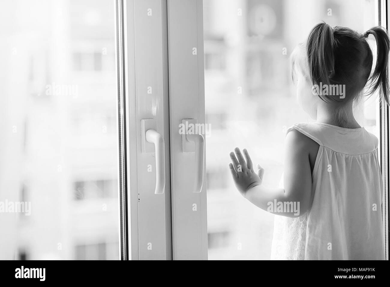 La bambina è seduta sul davanzale. Un mazzo di fiori in un vaso dalla finestra e una ragazza lo sniffing fiori. Una piccola principessa in un bianco dre Foto Stock