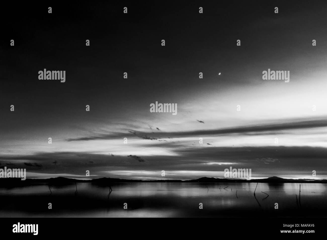 Bellissima vista del lago Trasimeno (Umbria, Italia) al tramonto, con toni del bianco e del nero e la luna nel cielo Foto Stock