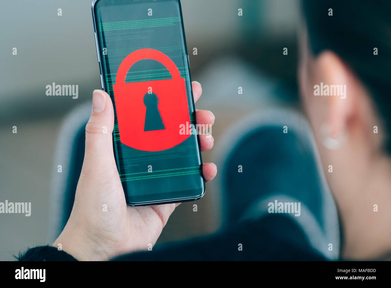 Al di sopra della spalla guardare di donna azienda smart phone dispositivo con schermo tecnico che mostra il codice sorgente e il lucchetto rosso Foto Stock