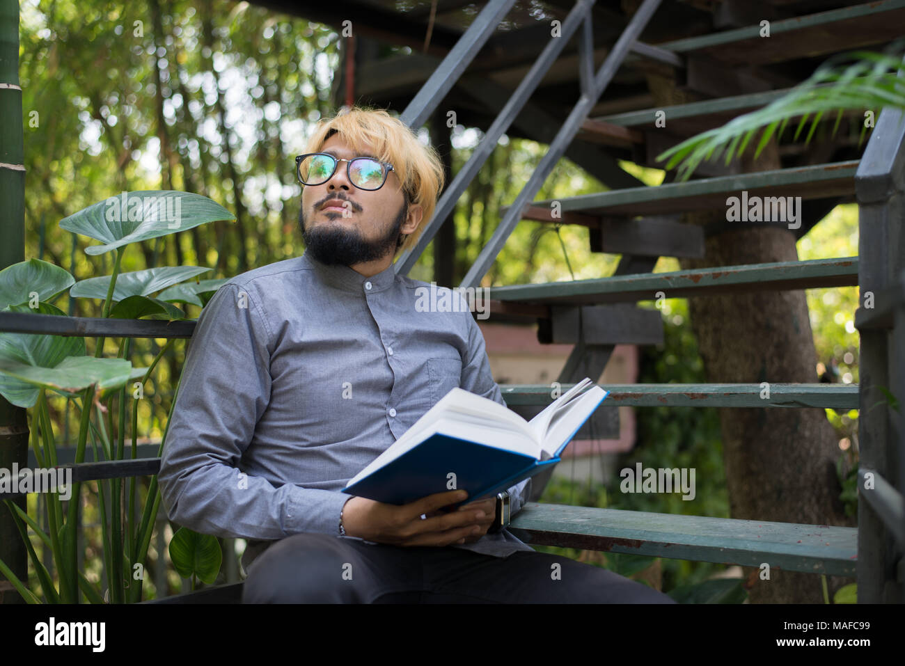 Giovani hipster barba uomo la lettura di libri nel giardino di casa con la natura. Il concetto di istruzione. Foto Stock