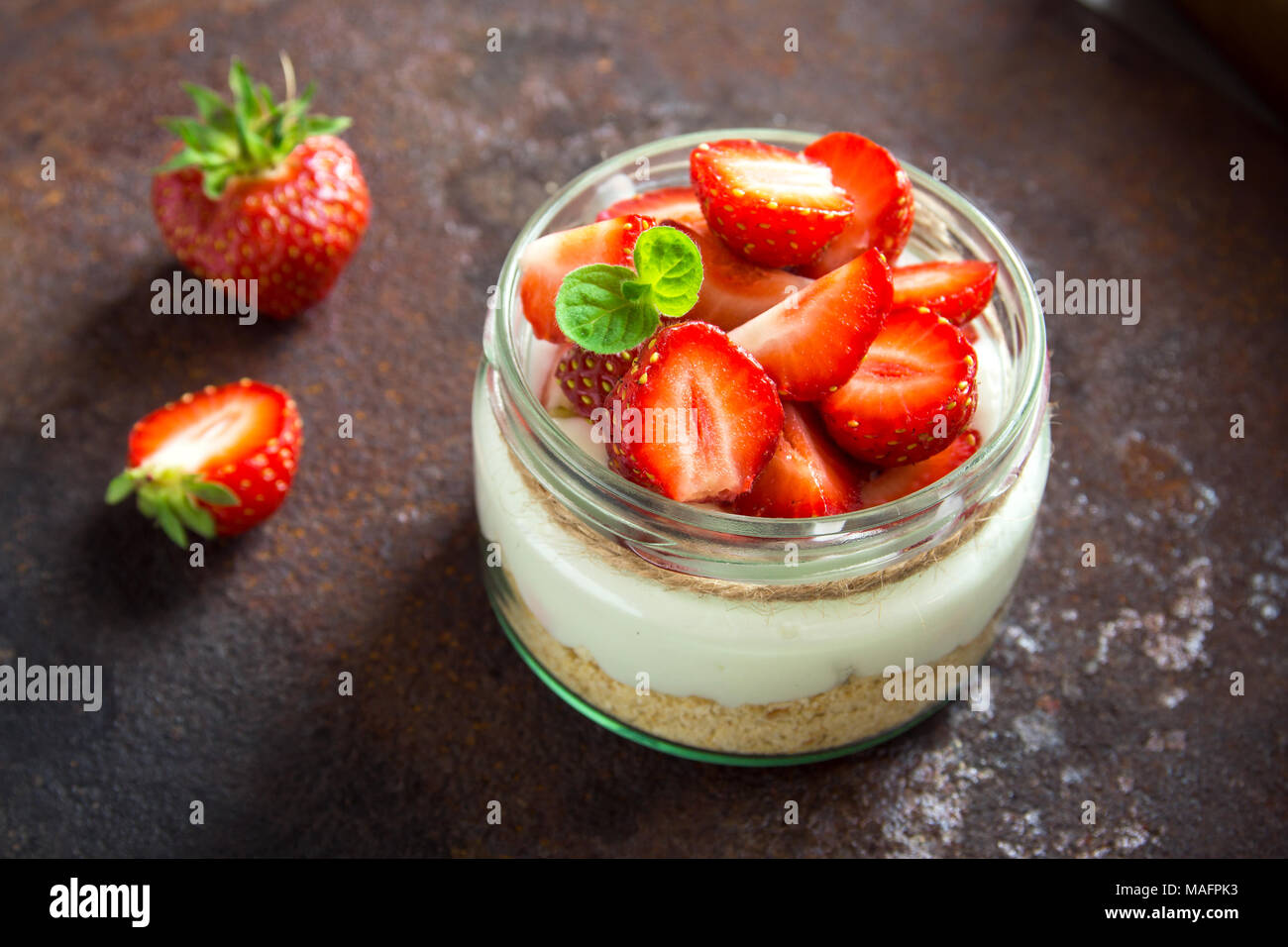 Strawberry Cheesecake in un barattolo di vetro con fragole fresche e crema di formaggio su sfondo scuro. Sana dessert fatti in casa. Foto Stock