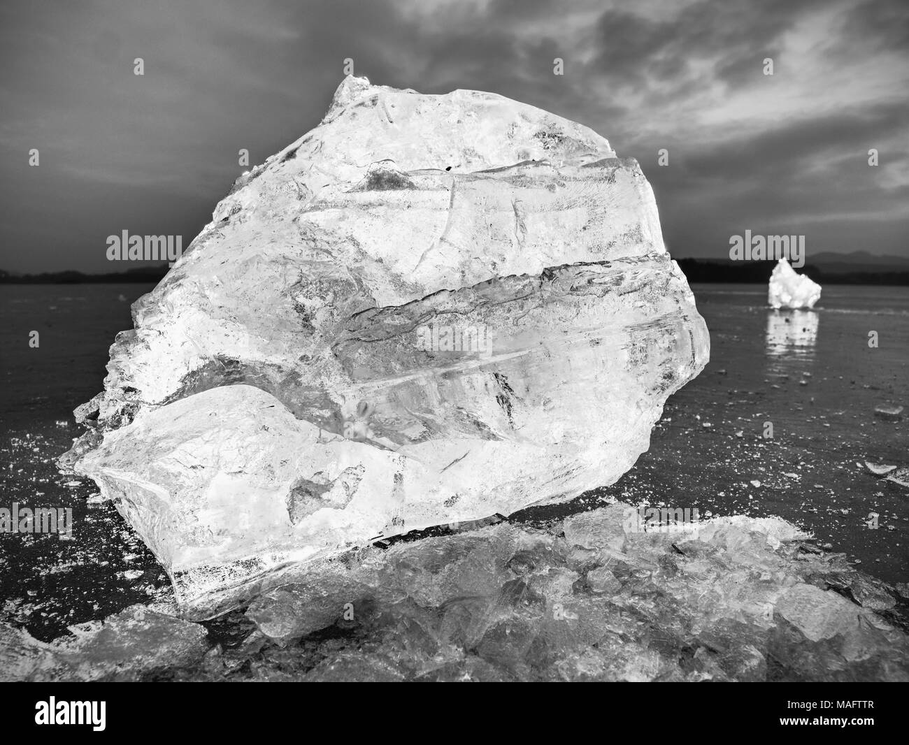 Cubetti di ghiaccio al buio su un suolo riflettente. Incandescente pezzi di ghiaccio tritato e fiocchi di neve in condizioni di forte retroilluminazione. La fotografia in bianco e nero. Foto Stock