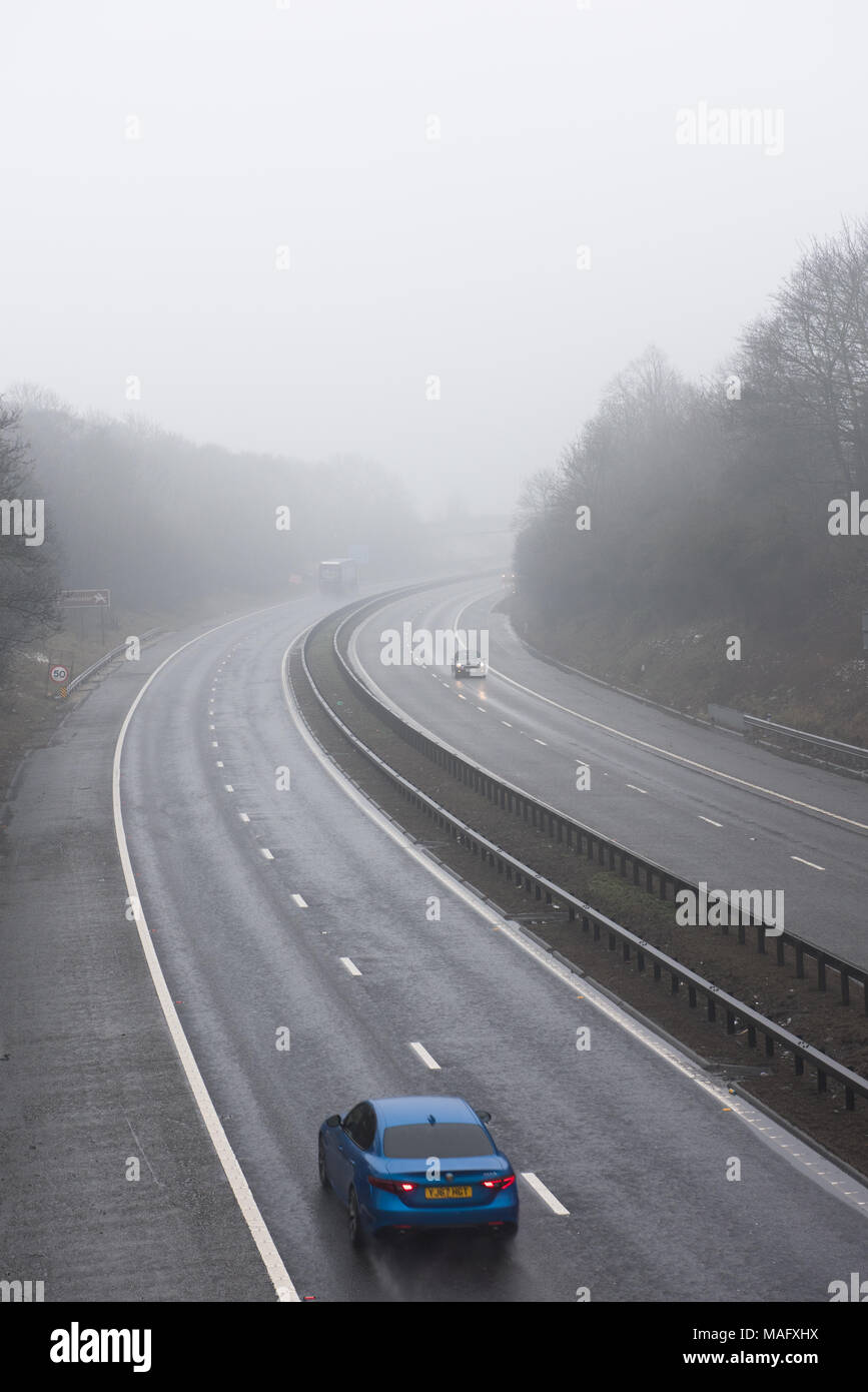 Autocarri e veicoli che percorrono un'autostrada britannica bagnata e nebbiosa, circondata da boschi. Condizioni meteorologiche tipiche del Regno Unito Foto Stock