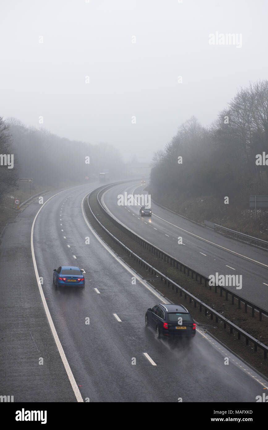 Autocarri e veicoli che percorrono un'autostrada britannica bagnata e nebbiosa, circondata da boschi. Condizioni meteorologiche tipiche del Regno Unito Foto Stock