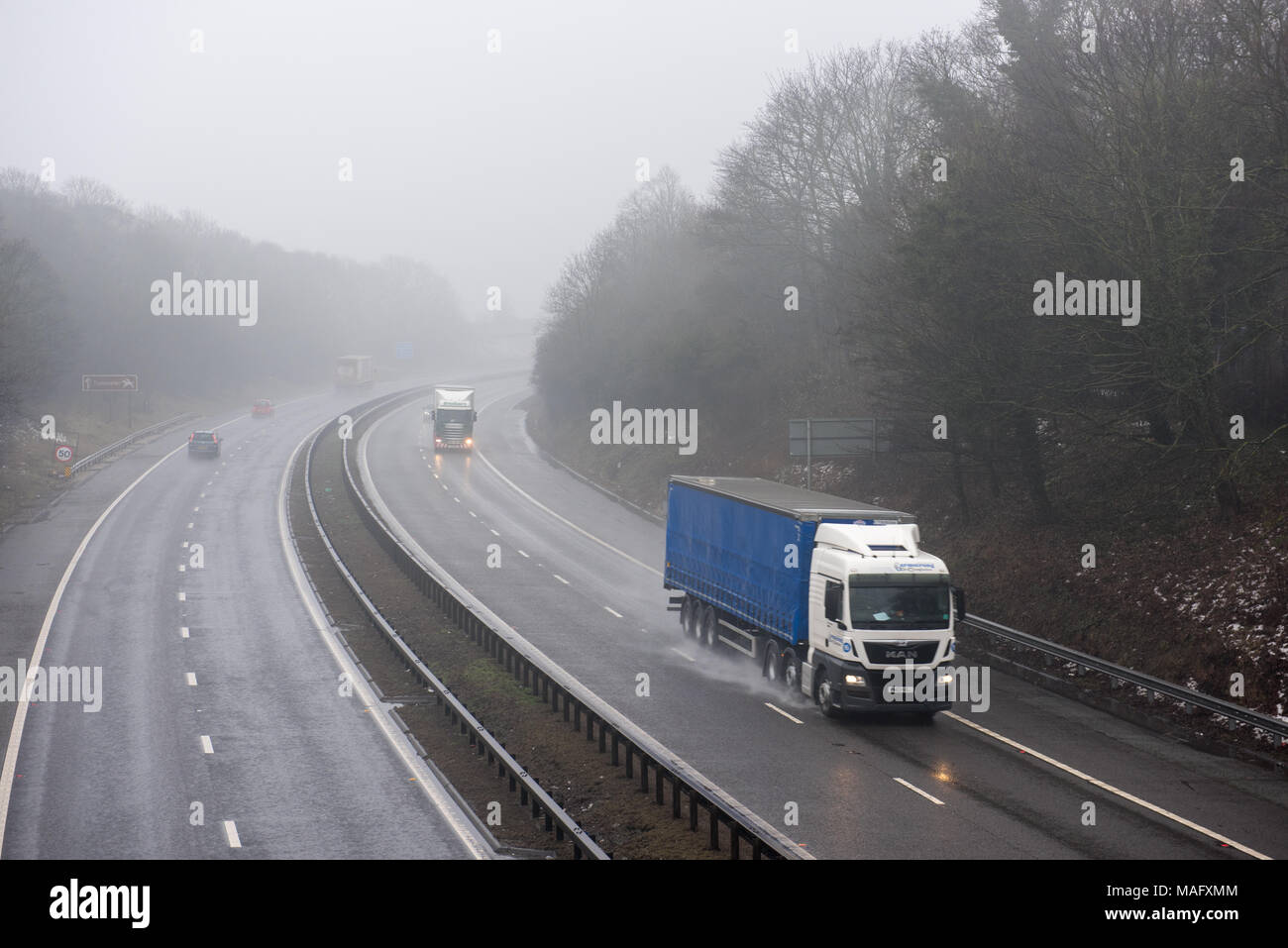 Autocarri e veicoli che percorrono un'autostrada britannica bagnata e nebbiosa, circondata da boschi. Condizioni meteorologiche tipiche del Regno Unito Foto Stock