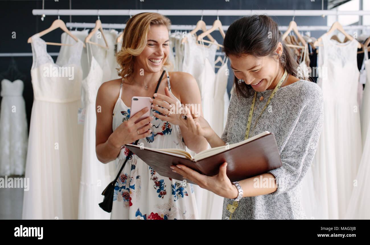 Client femmina nella boutique nuziale con tailor tenendo un diario. Designer di nozze con la donna il cliente in wedding fashion store. Foto Stock