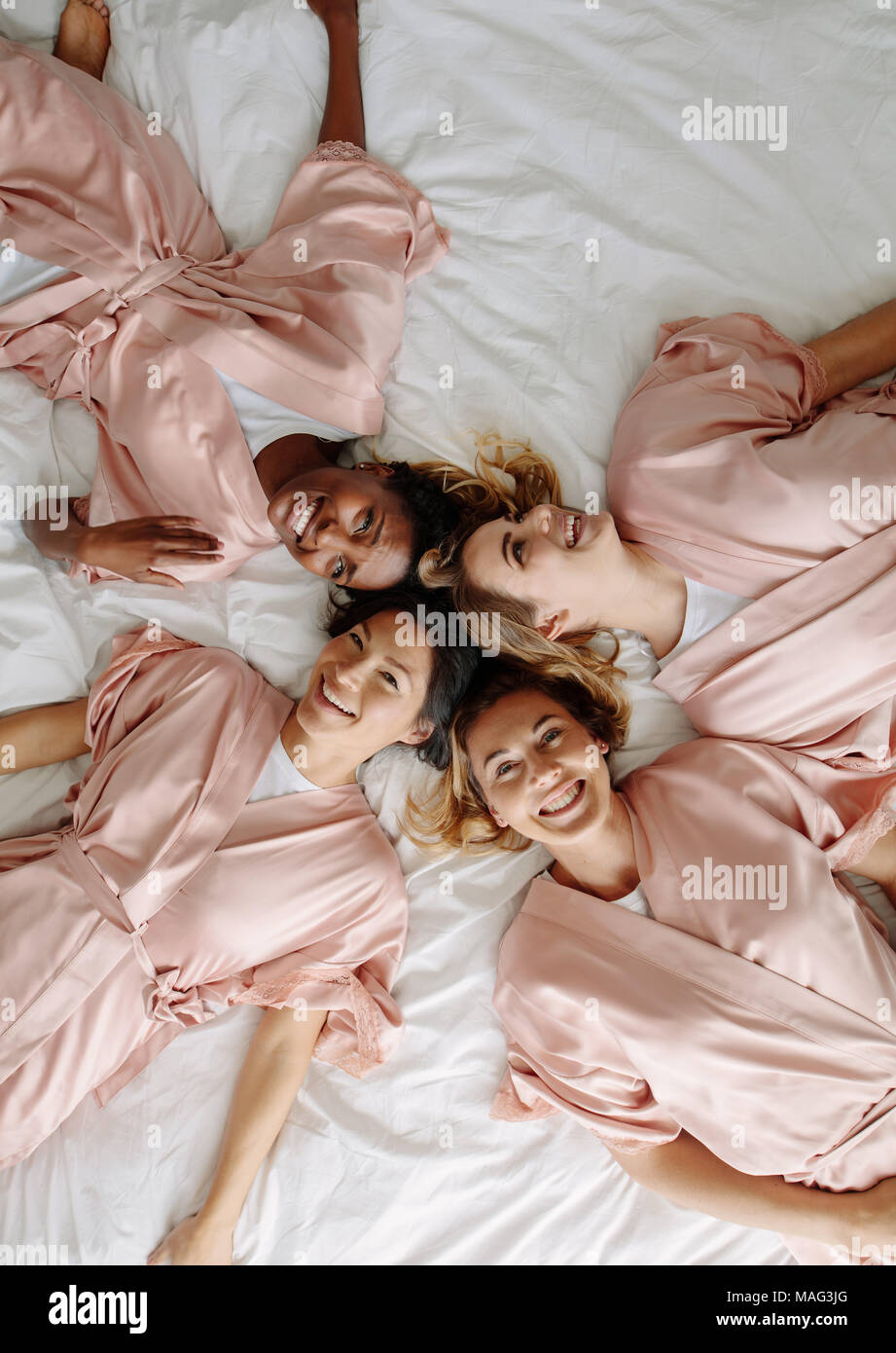 Vista superiore della sposa con bridesmaids sdraiato sul letto e sorridente. Un gruppo di donne che indossano tunica dormiente sdraiato sul letto di casa. Foto Stock