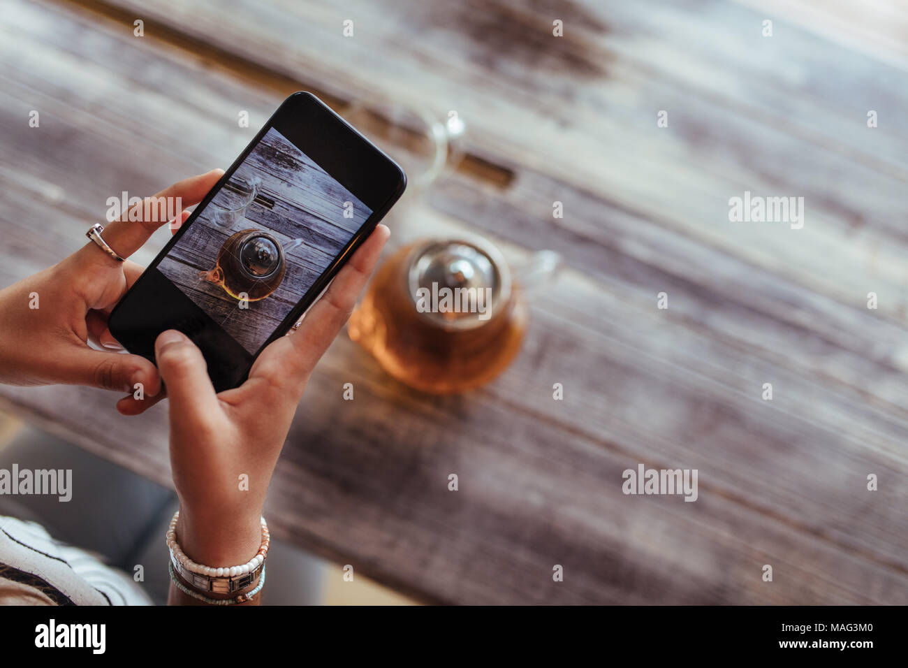 In prossimità di una donna di catturare foto di una teiera in vetro utilizzando un telefono cellulare per il suo cibo blog. Blogger alimentare a scattare foto per il suo blog. Foto Stock