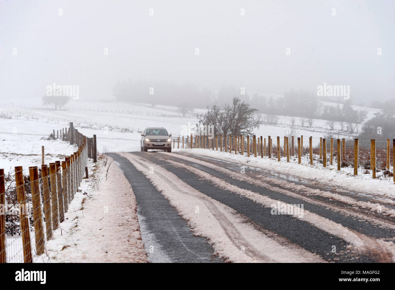 Builth Wells, Powys, Regno Unito. Il 2 aprile 2018. Un automobilista trascina lungo la B4520 (Brecon Road) circondato paesaggio invernale del Lunedì di Pasqua sul Mynydd Epynt gamma di circa 300 metri sopra il livello del mare vicino a Builth Wells. La neve è scesa la scorsa notte fino a circa 150 metri sopra il livello del mare in Powys, Wales, Regno Unito. © Credit: Graham M. Lawrence/Alamy Live News. Foto Stock