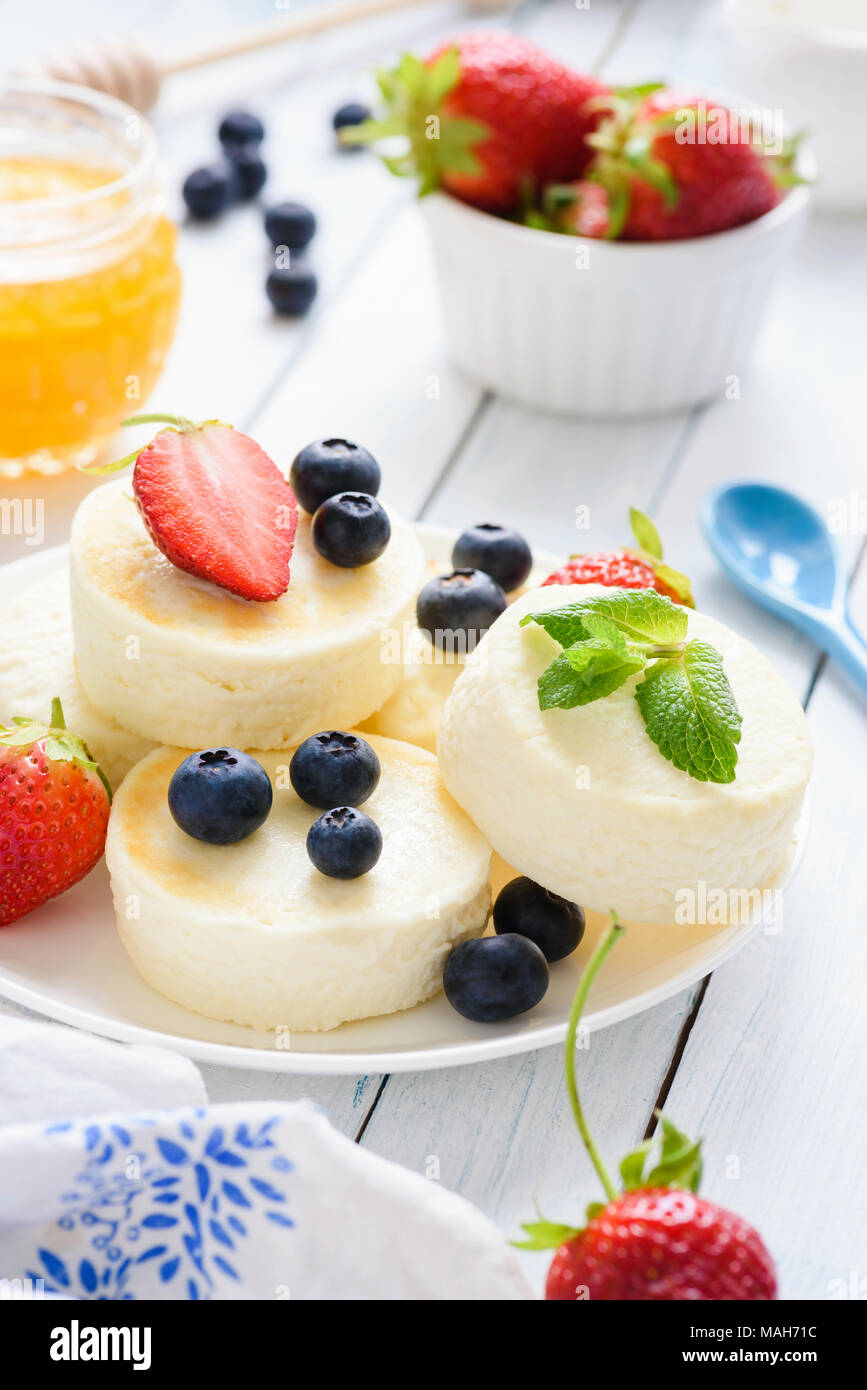 Mini cheesecake con frutti di bosco freschi e menta su sfondo bianco. Messa a fuoco selettiva Foto Stock