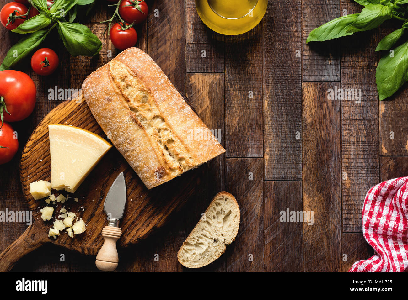 Il cibo italiano su legno rustico sfondo, vista dall'alto. Il formaggio parmigiano reggiano, ciabatta, bruschette, basilico, olio d'oliva e pomodori. Cucina italiana Foto Stock