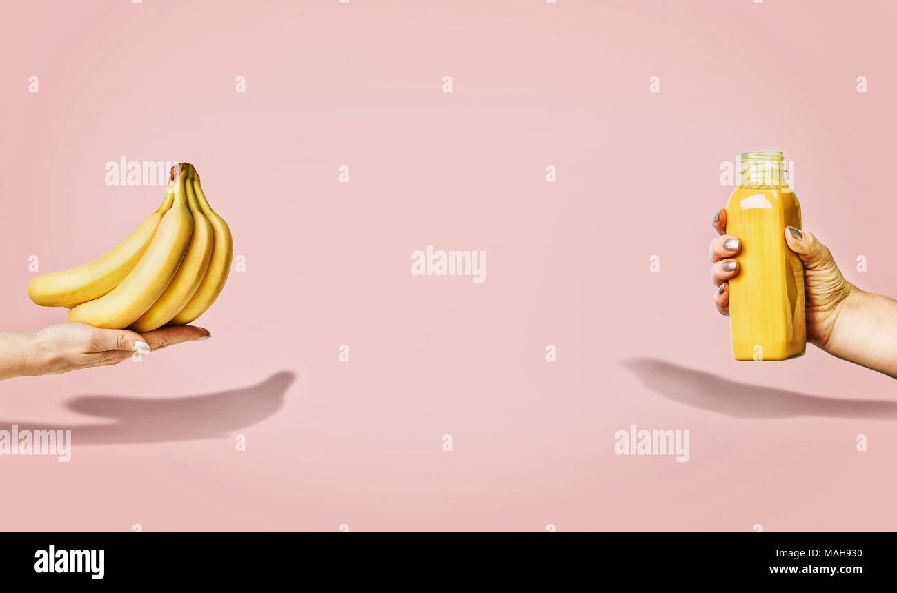 Estate cibo e bevande sfondo con banane e bere giallo bottiglia in mano femminile a pastello sfondo rosa, vista frontale, un banner o un modello. Foto Stock