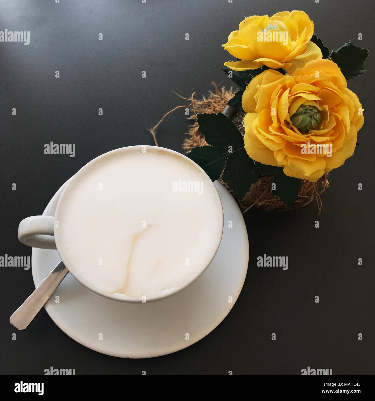 Tazza di caffè cappuccino su una tavola nera con rose giallo Foto Stock