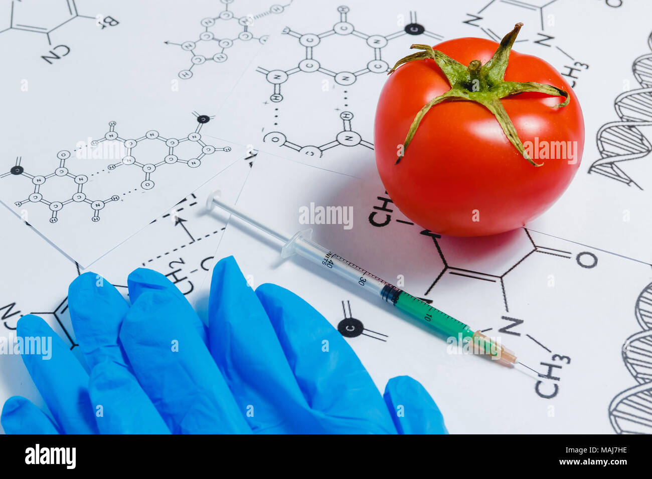 Concetto di Non-prodotti naturali, ogm. Siringa, guanti blu e rosso pomodoro su sfondo bianco con formula chimica, Foto Stock