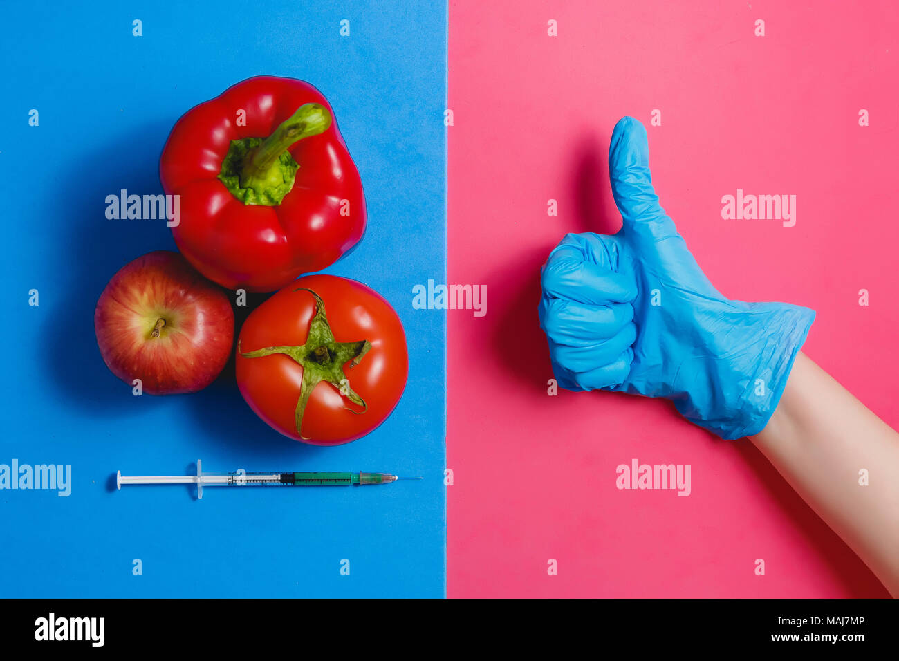 Il Pollice Verde liquido nella siringa, rosso pomodoro, Apple, pepe. Alimenti geneticamente modificati concetto su Rosa Blu. Foto Stock