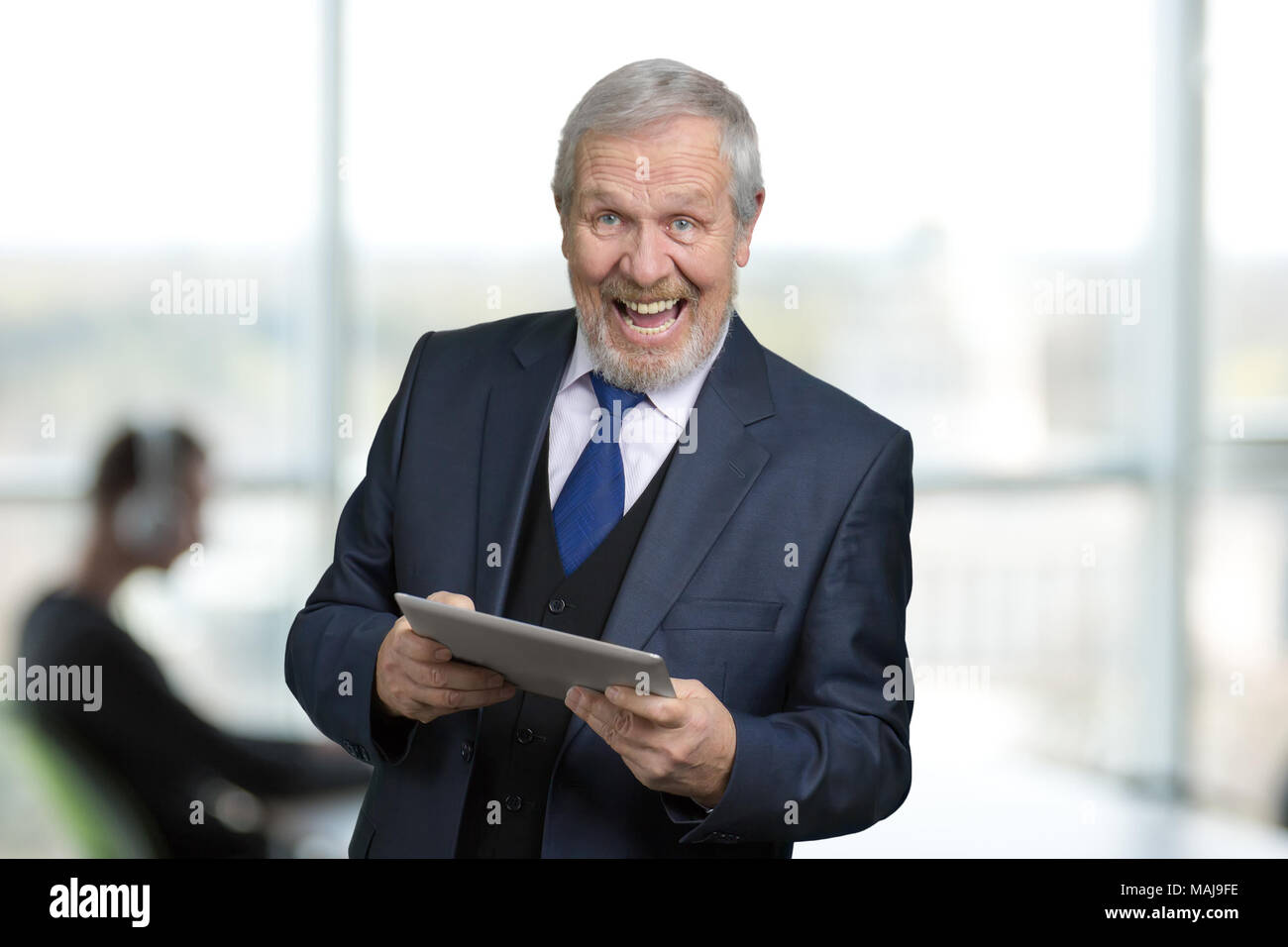 Estremamente felice l'uomo in tuta con tablet. Ritratto di gioia vecchio manager in ufficio. Finestre luminose sullo sfondo. Foto Stock
