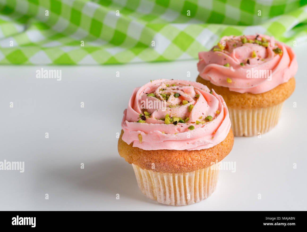 Due rosa rosa roteato frosted tazza di torte con pistacchio spruzza su sfondo bianco con spazio per il testo Foto Stock