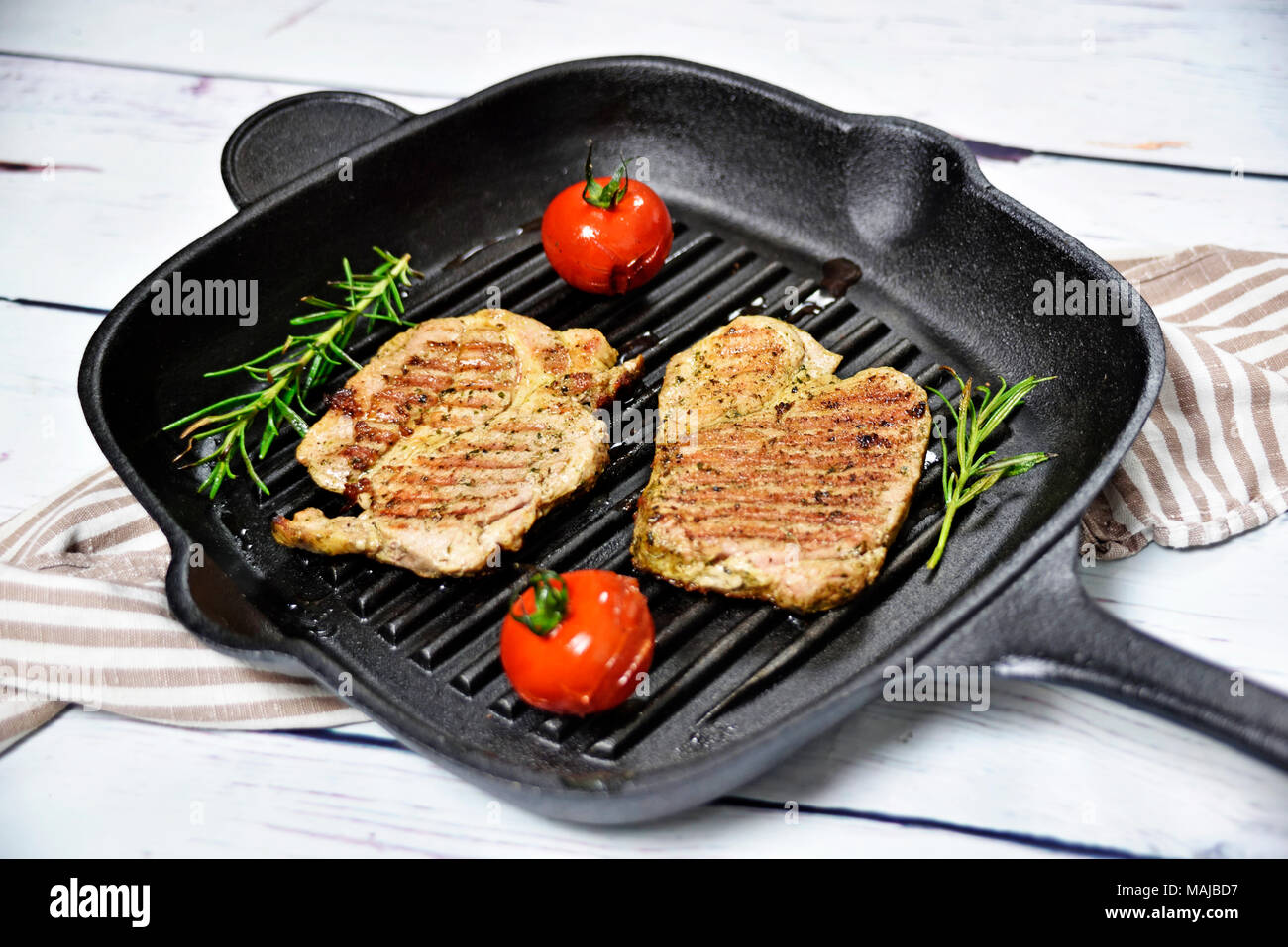 Le bistecche grigliate in una padella di ferro con pomodori e il ramo di rosmarino. Bistecche grigliate su un tavolo in legno, cucina gourmet. Foto Stock