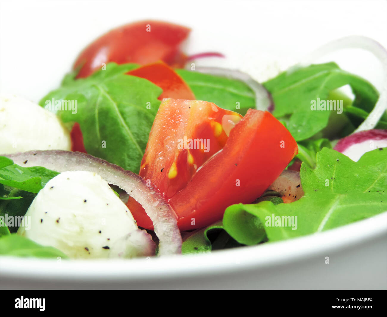 Gourmet o insalata fresca insalata caprese con pomodori, le cipolle rosse, rucola e mozzarella su una piastra bianca. Close-up shot di insalata fresca. Foto Stock