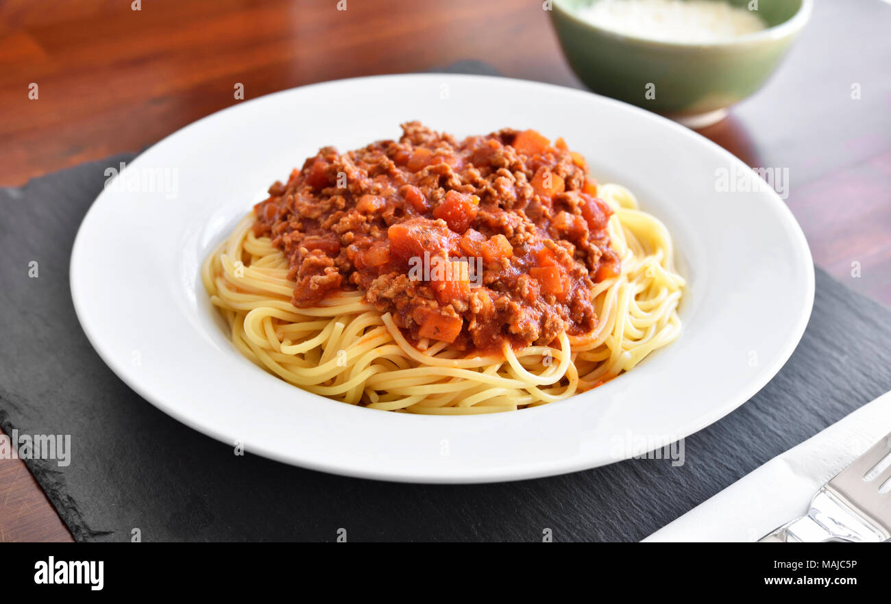 Deliziosa pasta pasto, spaghetti alla bolognese su una piastra bianca. Piatto di pasta, cibo tradizionale italiano con formaggio parmigiano, le carni macinate e le foglie di basilico. Foto Stock
