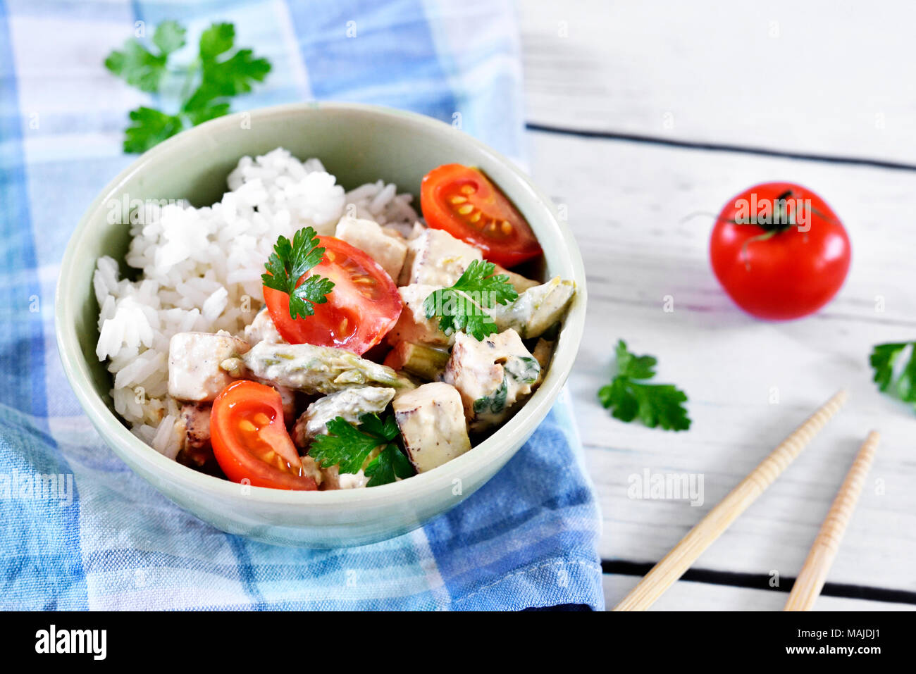 Delizioso piatto di tofu con il riso e i pomodori in una ciotola. Cibo Vegan con bacchette su un tavolo bianco. Stile di vita vegetariano. Foto Stock