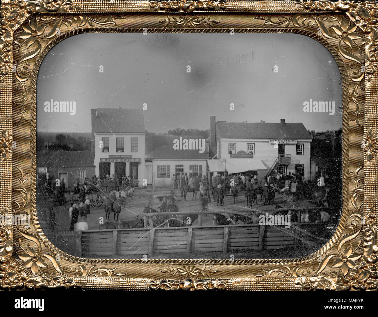 Molte persone, cavalli e carri lungo la strada principale di una città non identificato. Alcuni dei cavalli sono vincolati ad un palo vicino a un recinto in primo piano. Edifici commerciali la linea street e hanno segni sulla quale si possono leggere 'adattare', 'Howard House', 'DOC' e 'Drug e Prenota Store'. Alcuni individui pop la loro testa fuori della seconda storie di questi edifici commerciali. Titolo: Main Street nella città non identificato. . 1850. Thomas M. Orientale Foto Stock