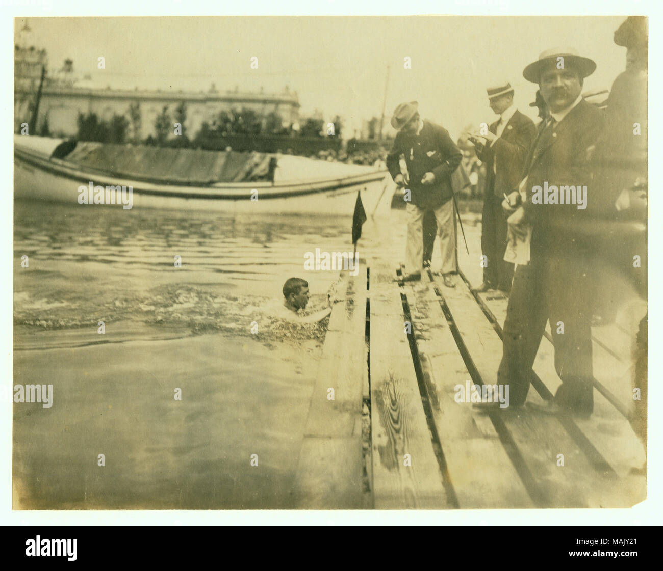 Fotografia orizzontale di un nuotatore di raggiungere una piattaforma, completando una gara. Ci sono dei giudici in piedi sulla piattaforma. Titolo: E. Rausche di Germania vincendo un miglio Campionato di nuoto, 1904 Olimpiadi. . 1904. Foto Stock