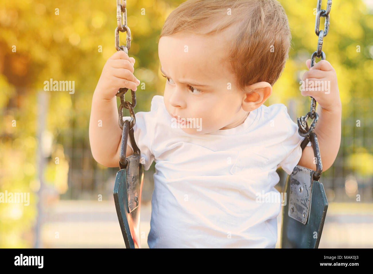 Carino baby boy divertirsi su altalena in un parco. Foto Stock