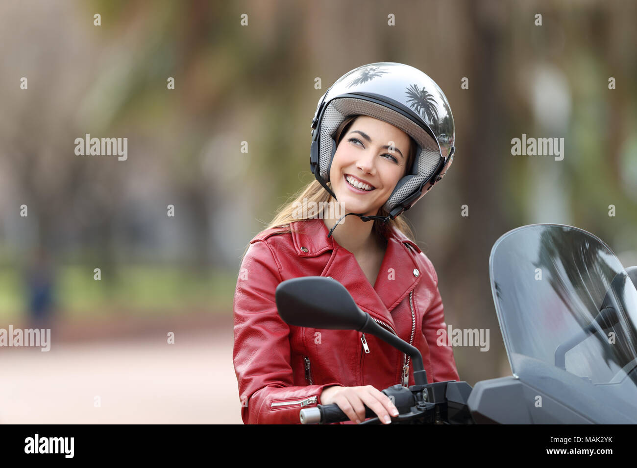 Felice biker indossando il casco seduto su una moto di sognare guardando al di sopra sulla strada Foto Stock