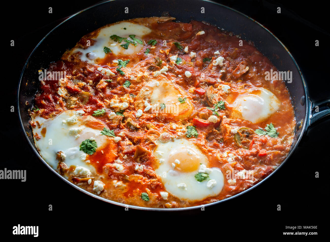 Gustosa e salutare Shakshuka, uova in camicia in pomodoro piccante salsa di peperoni , in una padella, su sfondo nero Foto Stock