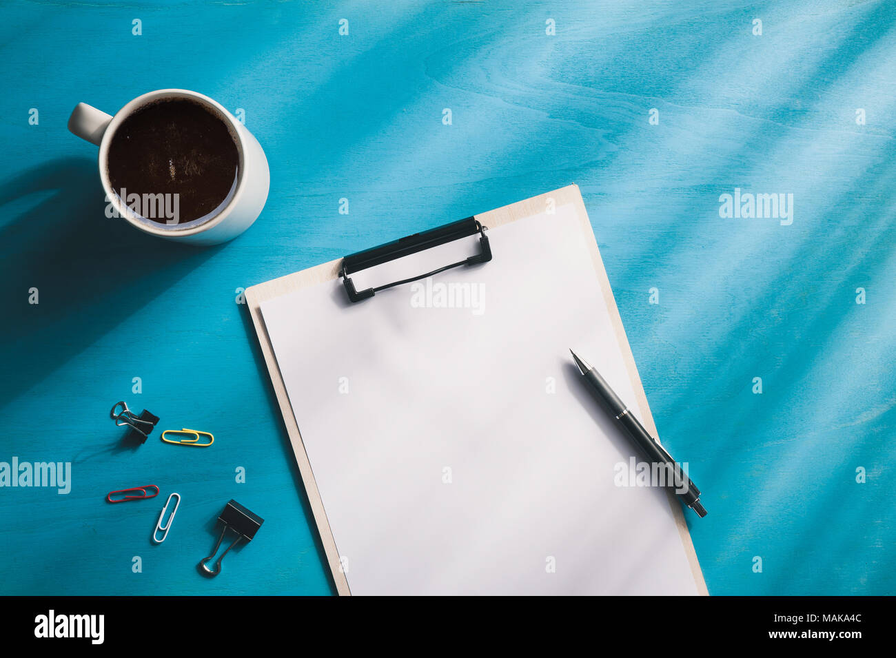 Dimensioni A4 negli appunti e una tazzina di caffè blu sulla tavola di legno con illuminazione naturale effetto nella mattina tempo. sfondo con la zona vuota per il testo o messaggio. Foto Stock