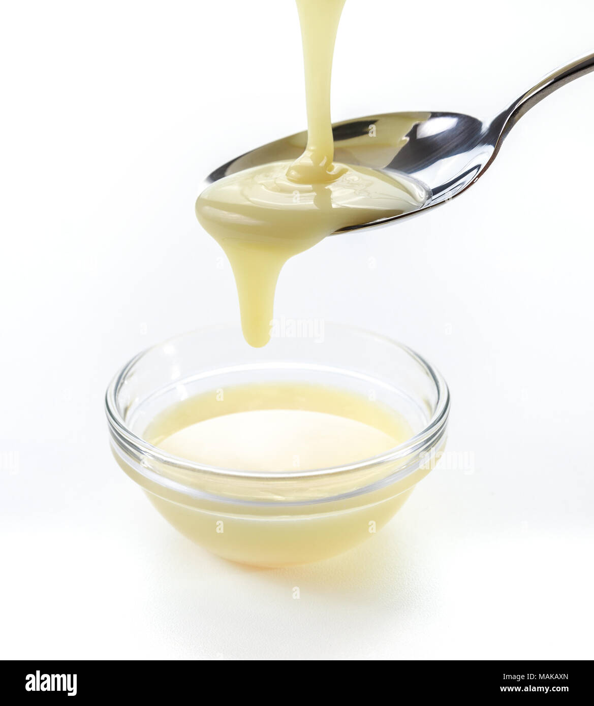Closeup versando il latte condensato con cucchiaino su sfondo bianco Foto Stock