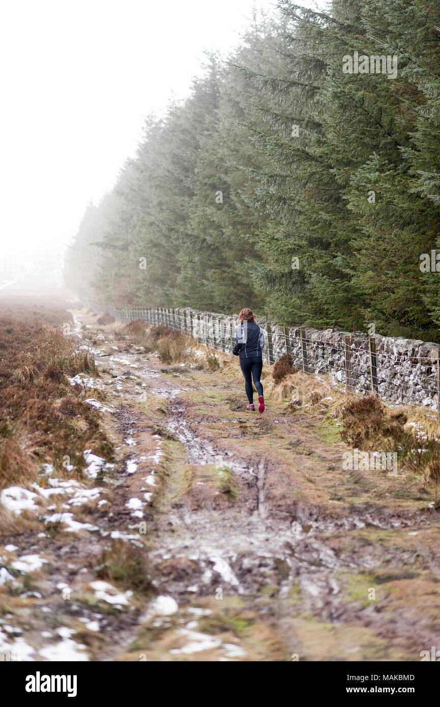 Una donna che corre lungo un fangoso sentiero forestale in condizioni di clima freddo Foto Stock