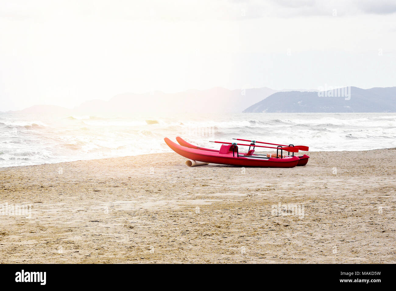 La luce diurna vista dal mare al rialzo le onde e le montagne sullo sfondo. Barca Rossa sulla sabbia con tracce di piede. Il cielo luminoso con le nuvole. Negativo dello spazio di copia Foto Stock