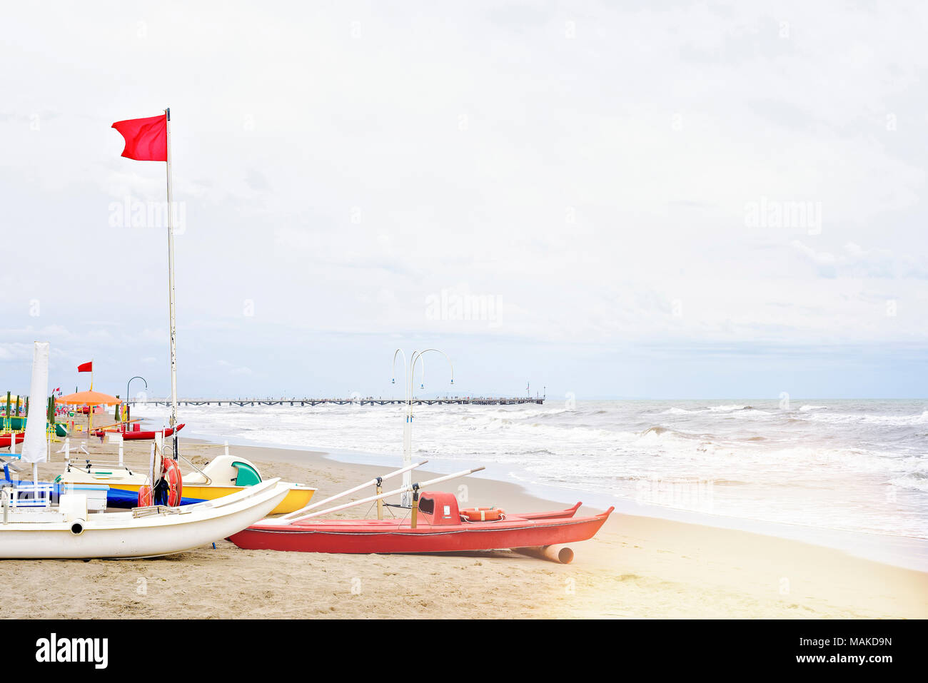 La luce diurna vista dal mare al rialzo le onde e pier su sfondo. Barche sulla sabbia con tracce di piede. Il cielo luminoso con le nuvole. Copia negativo spazio, luogo Foto Stock