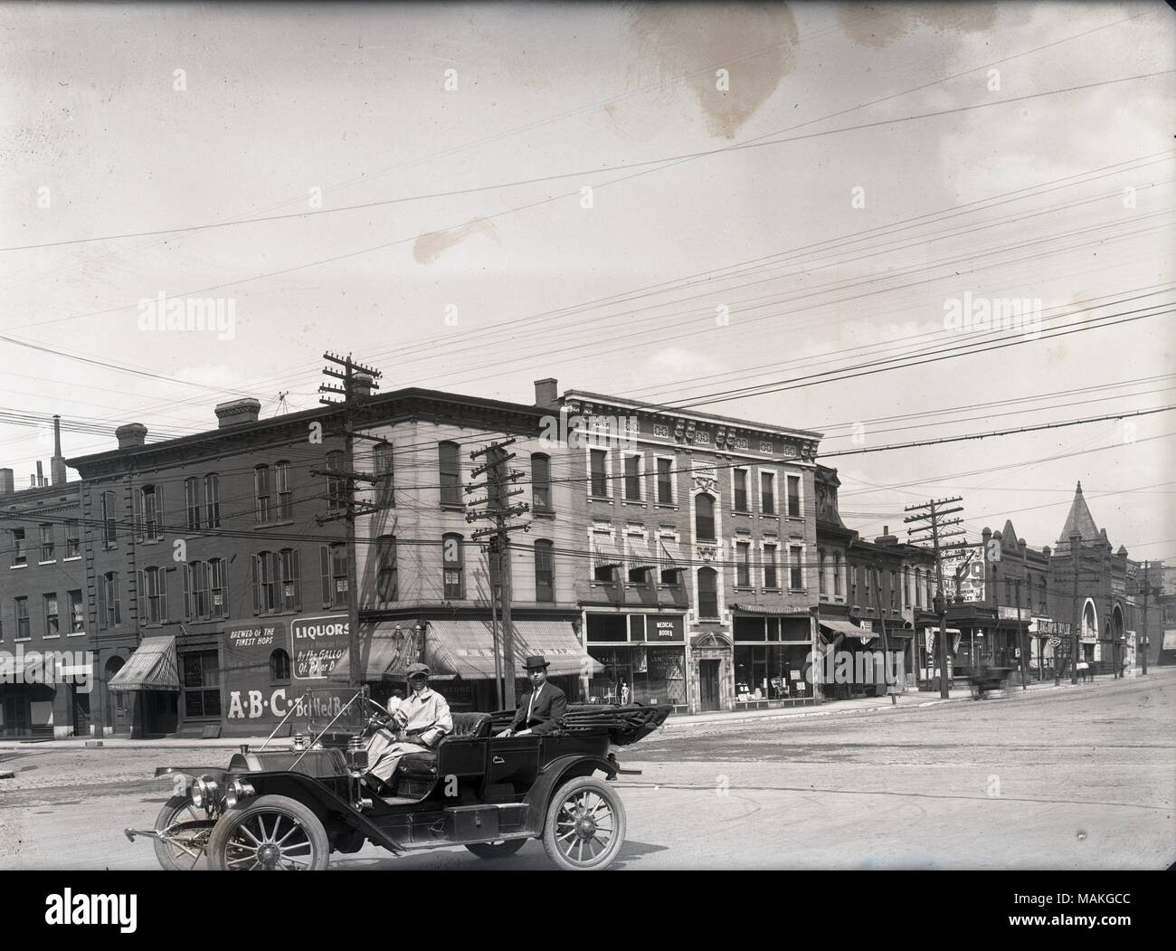 In orizzontale e di fotografia in bianco e nero che mostra due e tre piani edifici commerciali e residenziali a midtown. L'uomo essendo azionato da un autista in un aperto di automobili è in primo piano. Titolo: Olive Street tra Channing e il Cardinale strade. . 1911. Oscar Kuehn Foto Stock