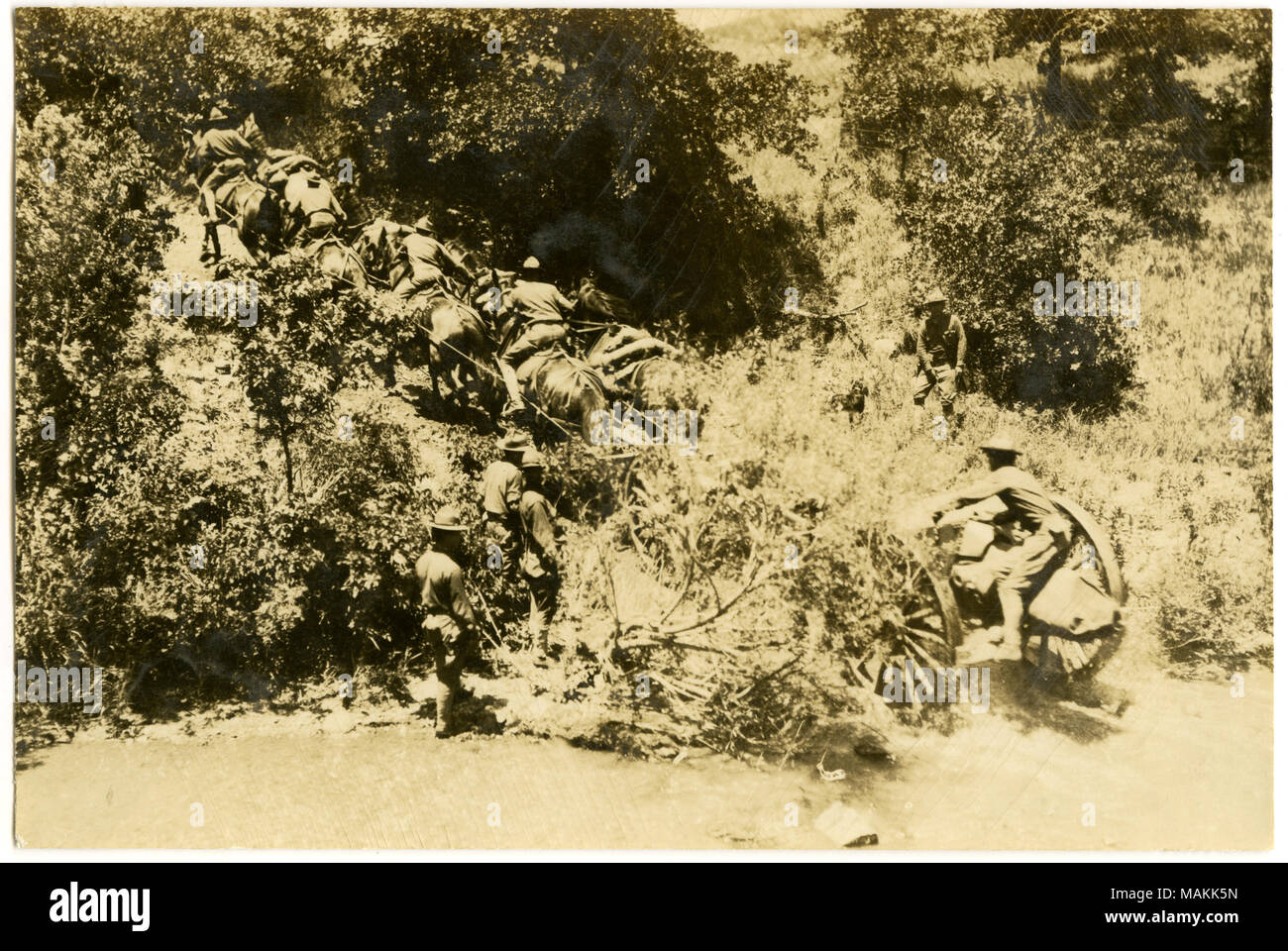 Orizzontale, seppia fotografia che mostra uomini in uniforme sia a cavallo e in piedi a terra su una collina vicino all'acqua. Gli uomini stanno usando i cavalli per tirare attrezzature su ruote fuori dall'acqua e su per la collina. Titolo: soldati tirando attrezzature su ruote fino alla cima di una collina. . Tra circa 1914 e circa 1918. Michel, Carl Foto Stock