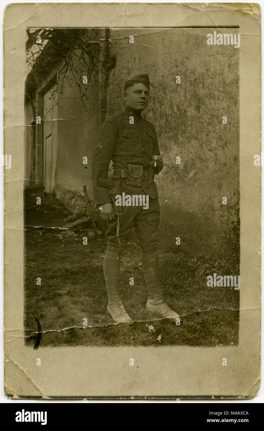 Verticale, seppia Cartolina che mostra un uomo in uniforme militare che posano per una foto di fronte a un muro di cemento, eventualmente parte di una casa o altri edifici. L'uomo è in possesso di una sigaretta nella mano sinistra. Una nota scritta sul retro della cartolina si legge: "Non molto buono, ma immagino che tu sai chi è." La cartolina potrebbe essere di origine francese. Titolo: soldato in uniforme che pongono di fronte a un muro di cemento per un'immagine. . Tra circa 1916 e circa 1918. Foto Stock