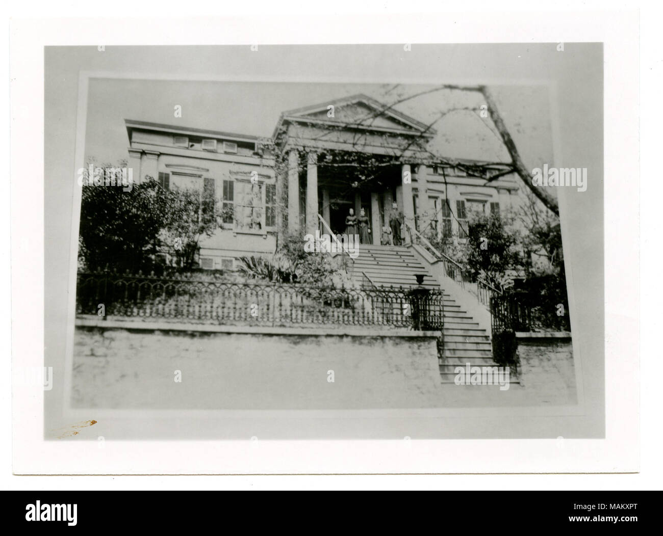 In orizzontale e di fotografia in bianco e nero di una storia di revival greco di pietra in stile residence con scalinata che conduce al portico anteriore. Un frontone triangolare è al di sopra del portico anteriore e sostenuto da colonne ioniche. Ante Telaio ciascuna finestra e due donne e un uomo e un bambino in piedi sulla parte anteriore portico. Titolo: Mincke, George Residence. 1709 Chouteau. . Tra circa 1870 e circa 1900. Swekosky, William G., 1895-1964 Foto Stock