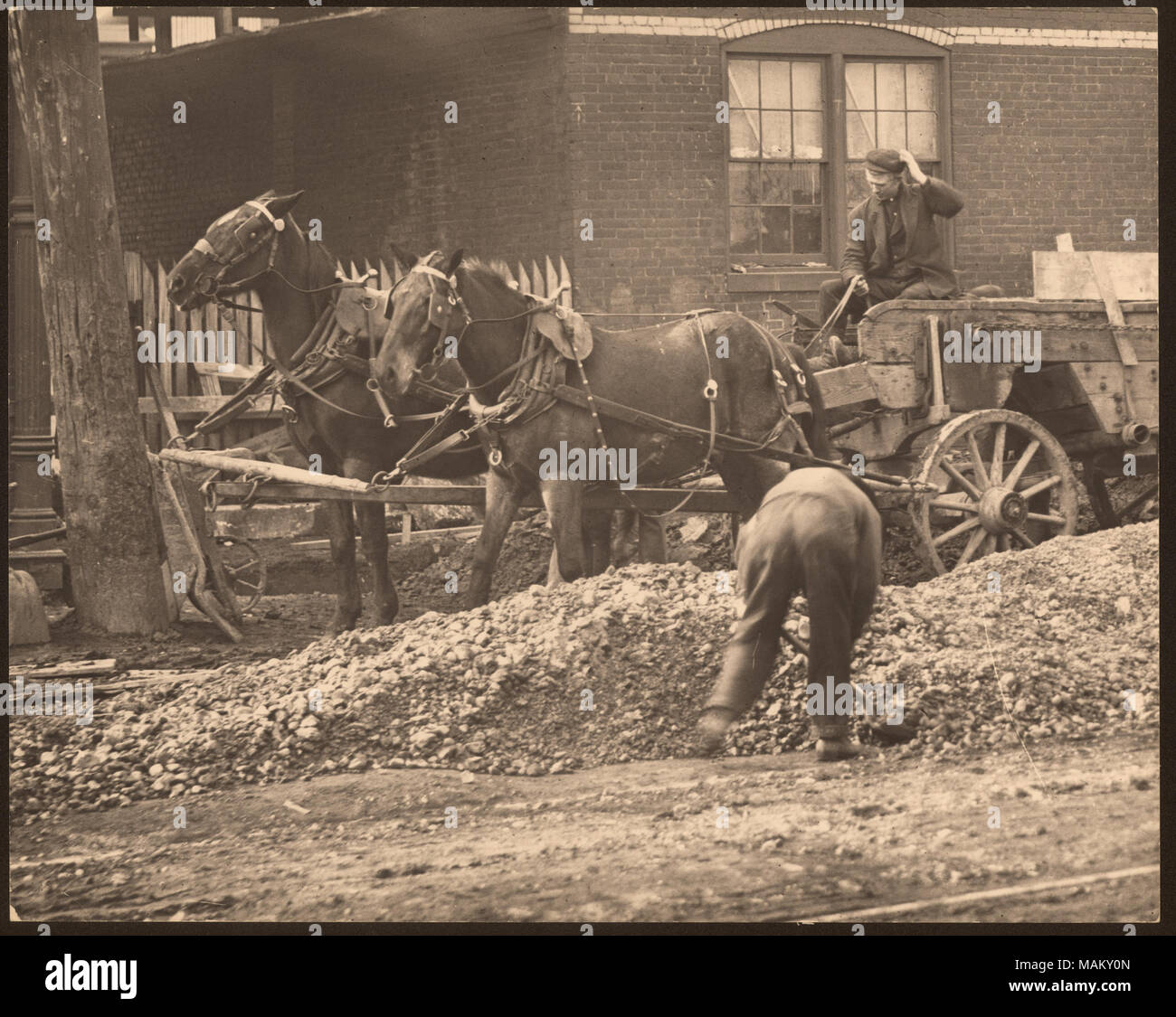 In orizzontale e di fotografia in bianco e nero di un vagone tirato da cavalli in un cantiere. Un uomo di badili e di sporco rock mentre un altro pilota il carro. Titolo: a cavallo il carro in mezzo a una strada non identificato sito in costruzione. . Tra circa 1800 e circa 1900. Swekosky, William G., 1895-1964 Foto Stock