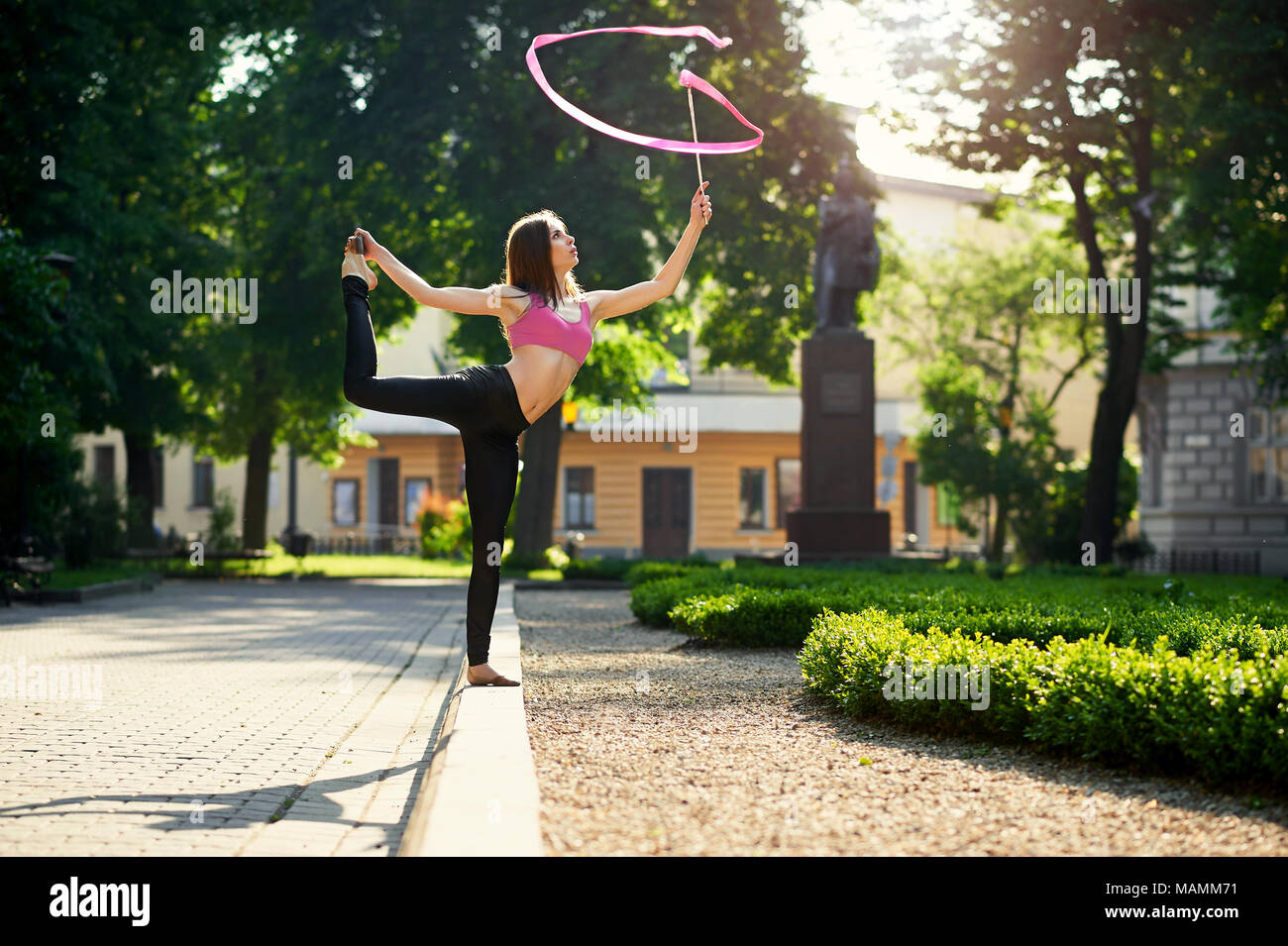 Ivano-Frankivsk, Ucraina - 1 Giugno 2015 : ragazza giovane con splendida figura sta ballando con nastro rosso in mattinata il parco della città. Donna in piedi sul letto giardino vicino impianti di verde. Foto Stock