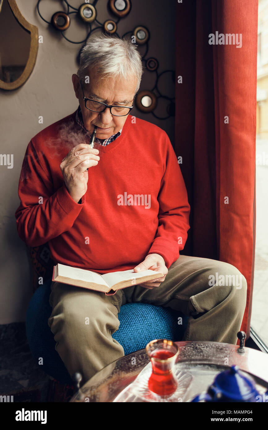 L'uomo anziano è seduto in cafe e la lettura di un libro. Foto Stock
