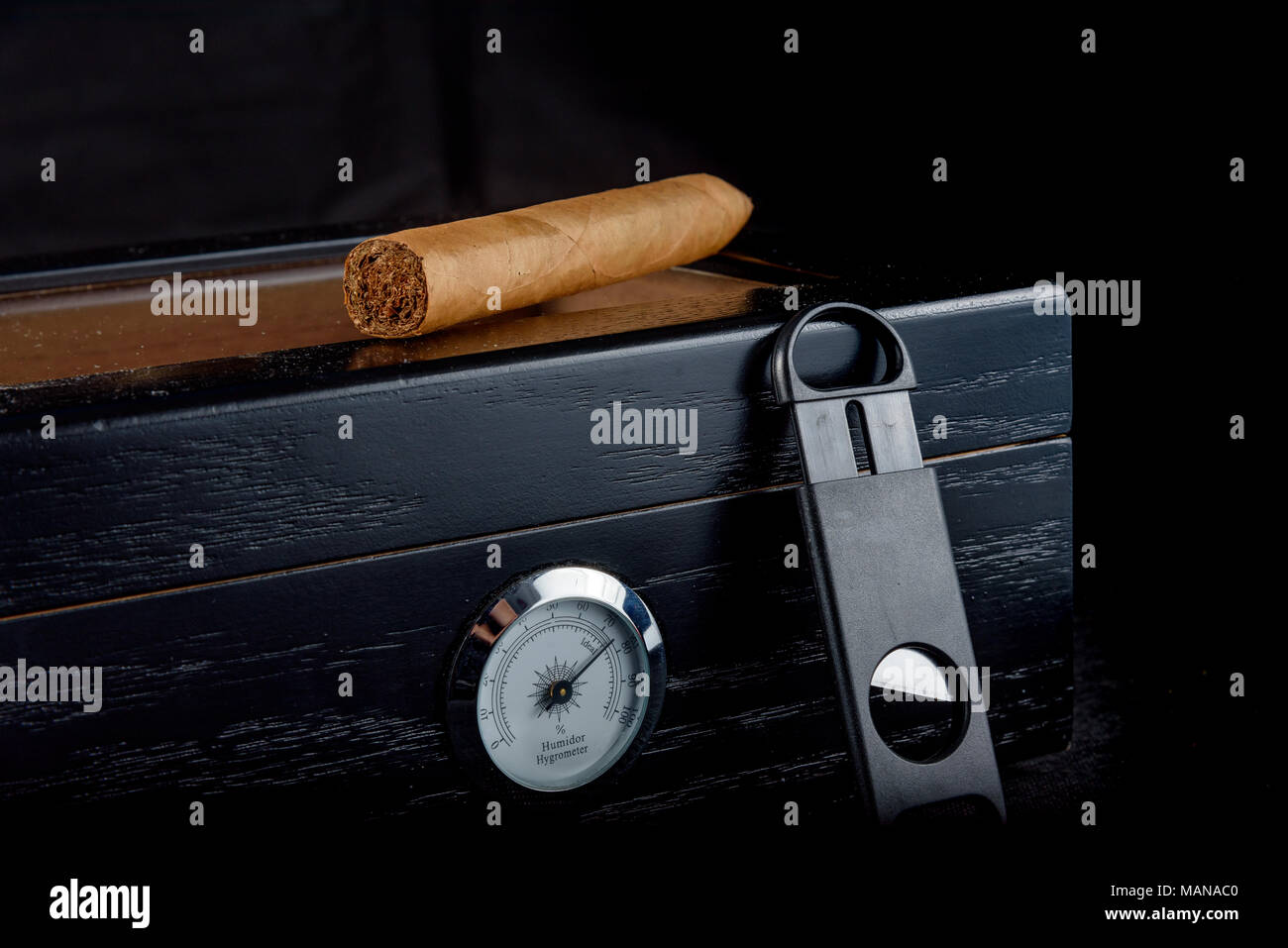 Un ricco odore di sigaro su un humidor nero accanto ad un rettilineo di coltello da caccia. Sfondo nero Foto Stock