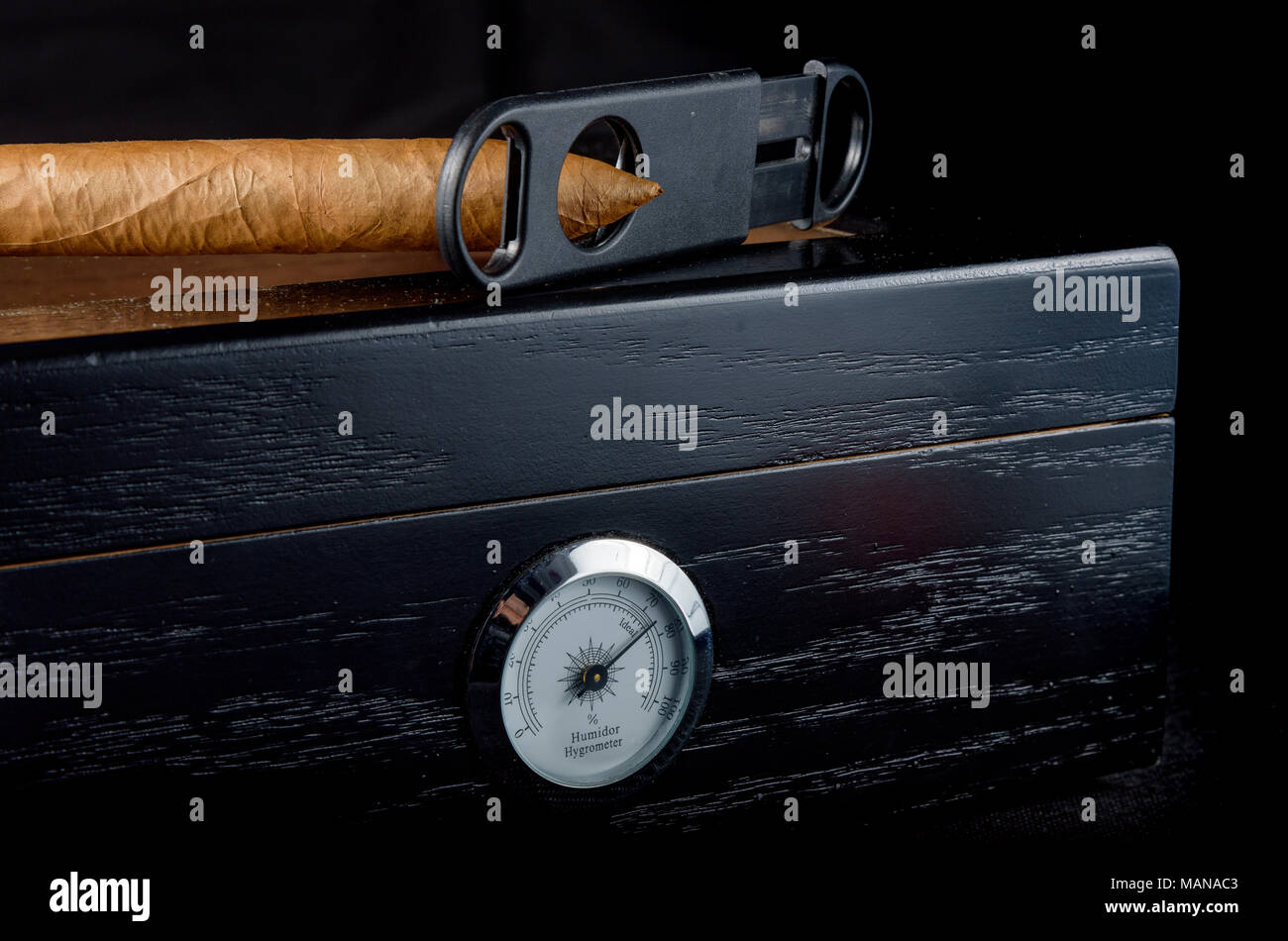 Un ricco odore di sigaro su un humidor nero accanto ad un rettilineo di coltello da caccia. Sfondo nero Foto Stock